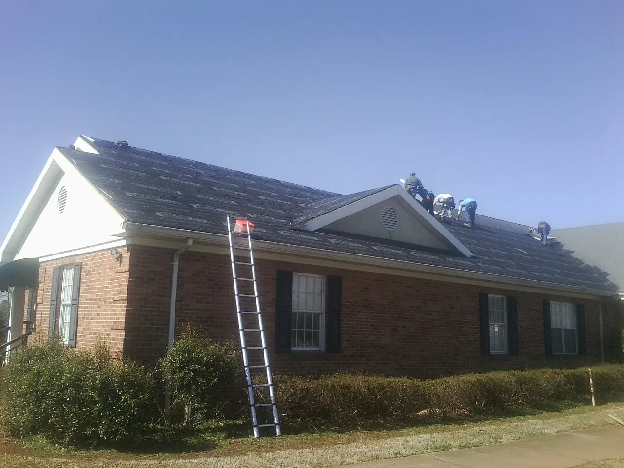 Crew tearing shingles off a brick ranch roof with a ladder set — Emergency Roof Repair work by our crew in Elko