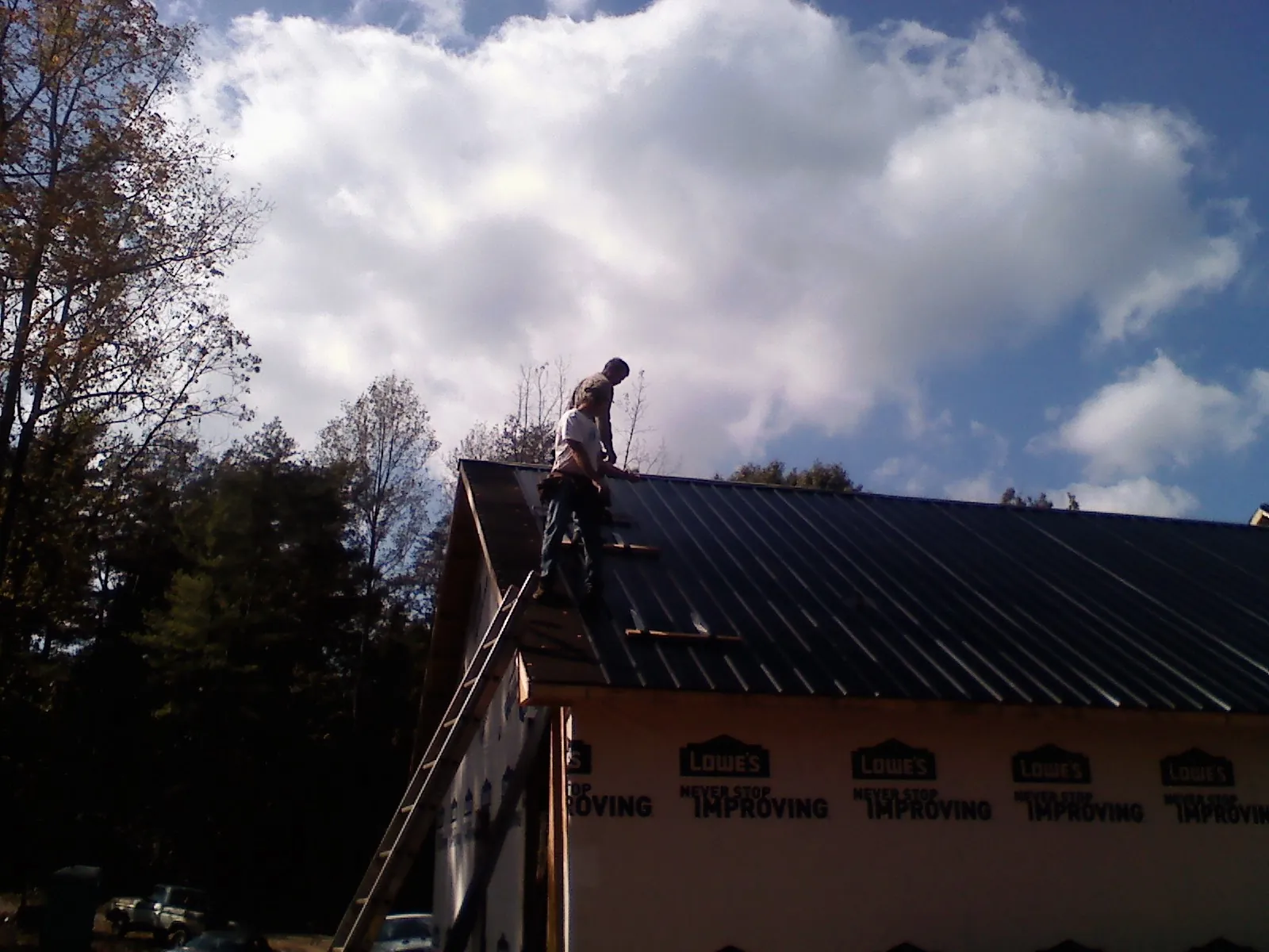 Roofer fastening dark metal panels high against a cloudy sky, from a Roof Inspection job in Elko