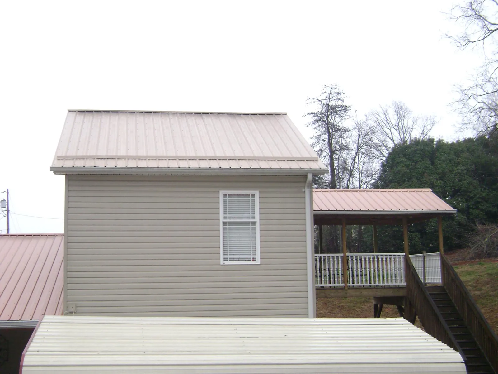 Tan metal roofs on a two story addition and attached porch, from a Roof Replacement job in Elko